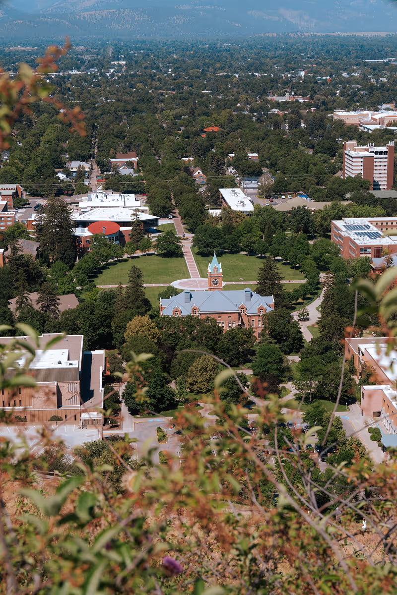 Aerial view of a university campus with a central clock tower building surrounded by green lawns and trees.