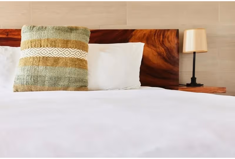 Bed with white linens, a striped decorative pillow, and a wooden headboard next to a nightstand with a lamp.