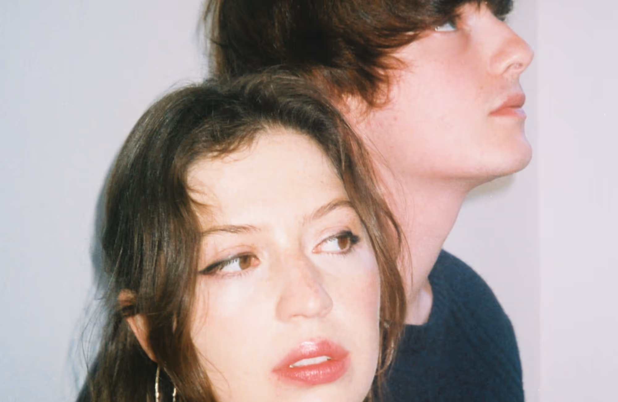 Close-up of a woman with long brown hair and glossy lips looking sideways and a man with short brown hair gazing upward.